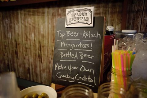 Chalkboard with saloon drink specials: Tap Beer, Margaritas, Bottled Beer, and 'Make Your Own Cowboy Cocktail.