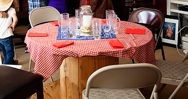 Saloon-Style Table Decoration Rustic saloon-style table decoration with a red gingham tablecloth, centerpiece, glass mugs, and red napkins.