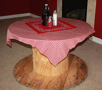 Rustic Saloon-Style Table with Gingham Tablecloth Rustic table covered with a red gingham tablecloth and a bandana centerpiece, holding a bottle and a candle.