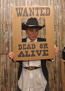 WANTED' Frame Photo at Murder Mystery Party Person in Old West attire holding a 'WANTED: DEAD OR ALIVE' frame, posing for a fun murder mystery party photo.
