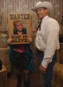 Old West Guests at Murder Mystery Party Two guests in Old West costumes, one holding a 'WANTED' frame, posing at a murder mystery party.